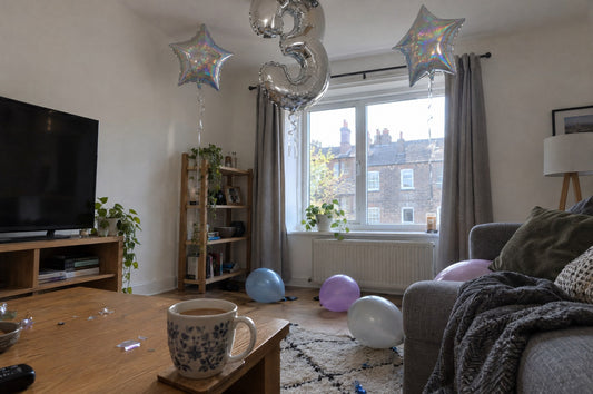 Living room the day after a party with foil star and number balloons still floating and latex balloons on the floor
